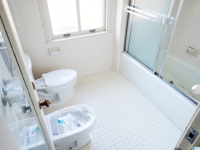 bathroom with tile patterned floors, combined bath / shower with glass door, toilet, and tile walls