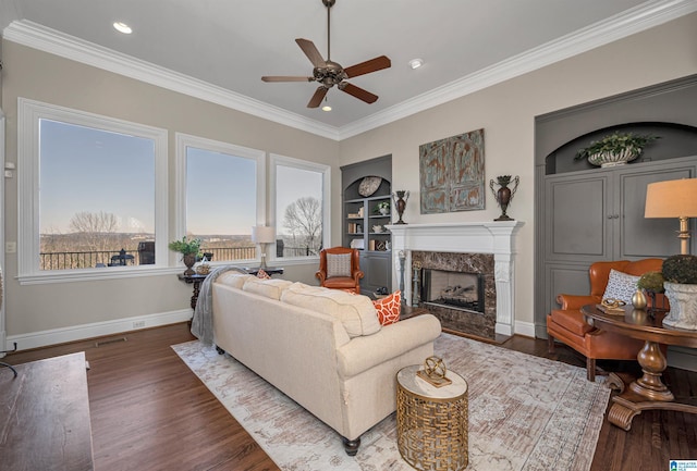 living area with built in features, wood finished floors, a fireplace, crown molding, and baseboards