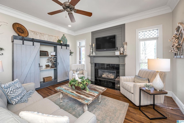 living room with a barn door, plenty of natural light, wood finished floors, and crown molding