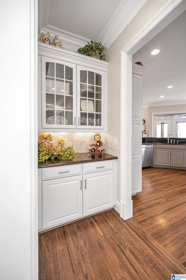 bar with stainless steel dishwasher, a sink, dark wood-style flooring, and ornamental molding