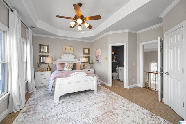 bedroom with crown molding, baseboards, a tray ceiling, light carpet, and ensuite bath