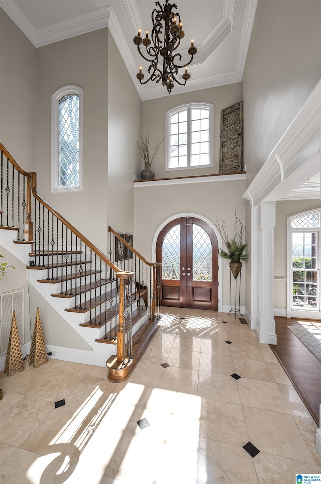 tiled entrance foyer featuring baseboards, stairway, ornamental molding, french doors, and a notable chandelier