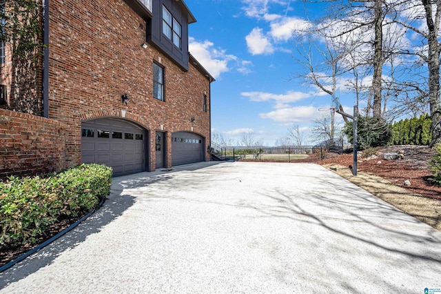 view of side of home with brick siding, an attached garage, driveway, and fence