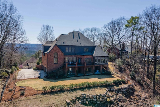 back of property with a fenced front yard, a yard, a sunroom, brick siding, and stairs