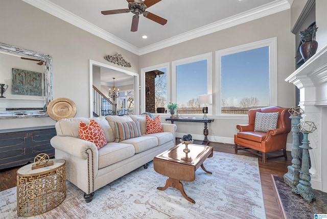 living area featuring baseboards, wood finished floors, ornamental molding, and ceiling fan with notable chandelier