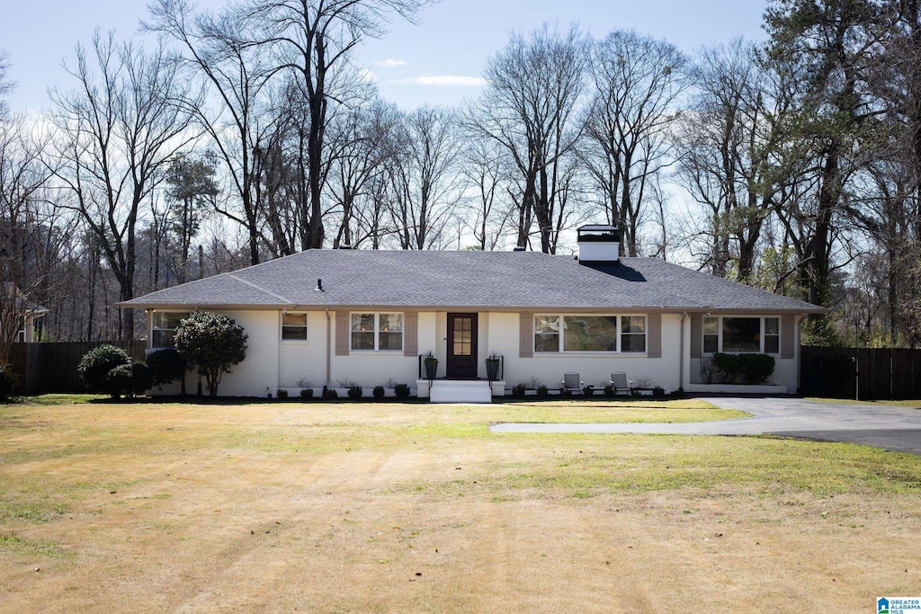 ranch-style house featuring a front yard, fence, and a chimney