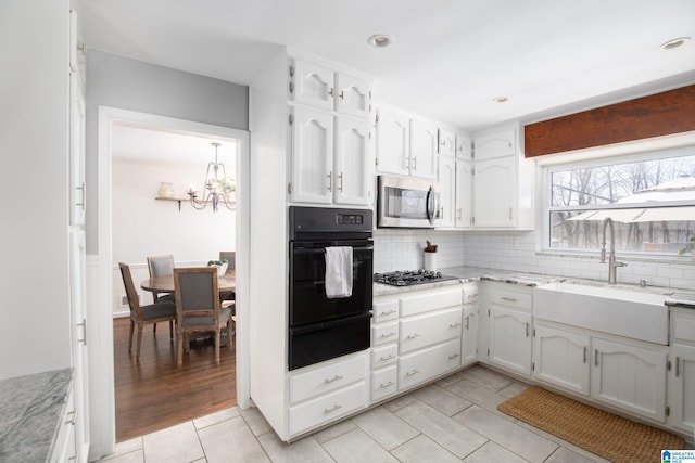 kitchen with stainless steel microwave, black oven, gas stovetop, a warming drawer, and a sink