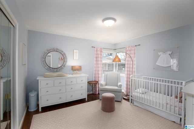 bedroom with a closet, a nursery area, and dark wood finished floors