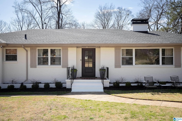 view of front of home with brick siding, a chimney, a front lawn, and a shingled roof