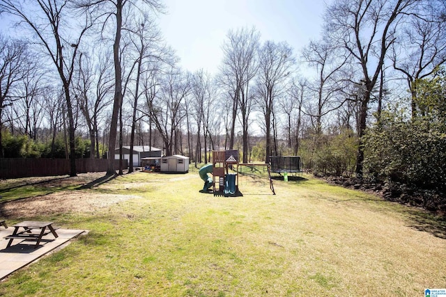 view of yard with a storage unit, a trampoline, fence, a playground, and an outdoor structure