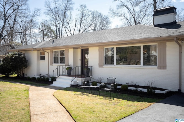 view of front of house featuring brick siding, a chimney, a front lawn, and a shingled roof