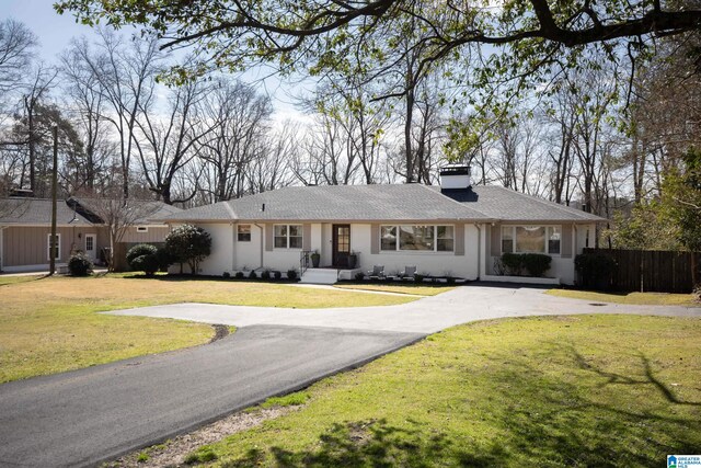 ranch-style home with a front lawn, fence, stucco siding, a chimney, and driveway