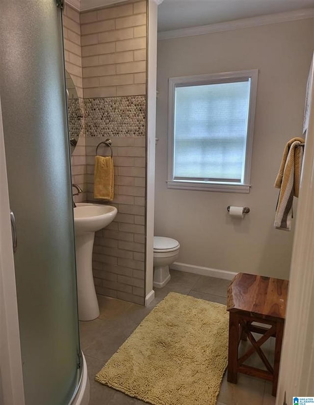 bathroom with a shower stall, crown molding, toilet, tile patterned floors, and tile walls