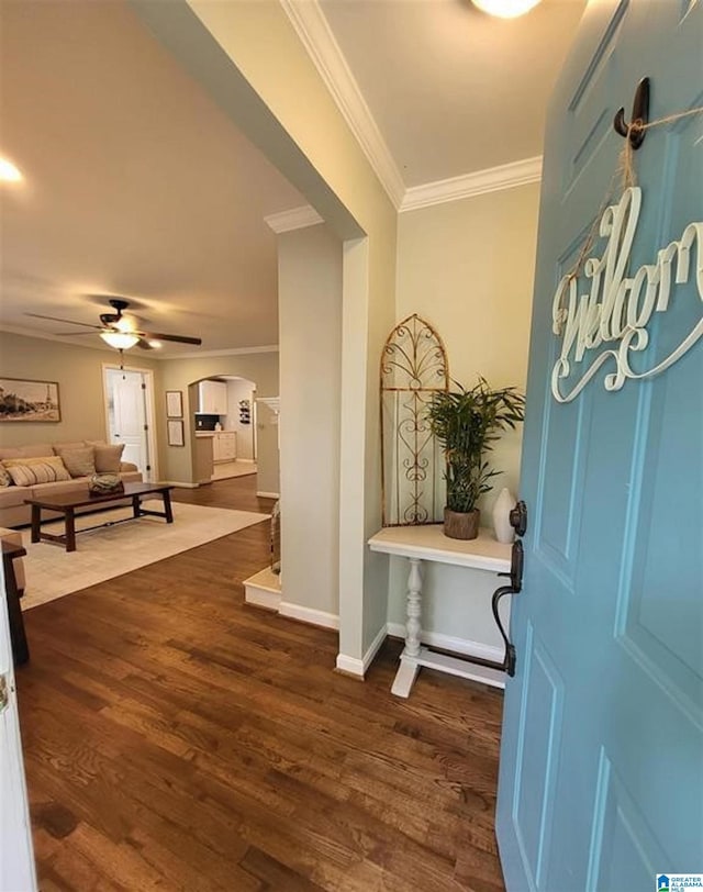 entryway featuring wood finished floors, arched walkways, crown molding, baseboards, and ceiling fan