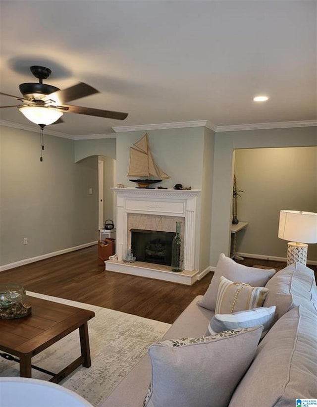 living area featuring baseboards, a premium fireplace, ornamental molding, wood finished floors, and a ceiling fan