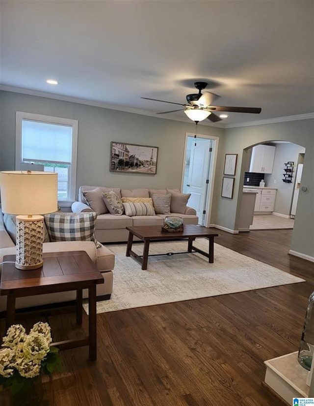 living room with ceiling fan, baseboards, ornamental molding, arched walkways, and dark wood-style flooring