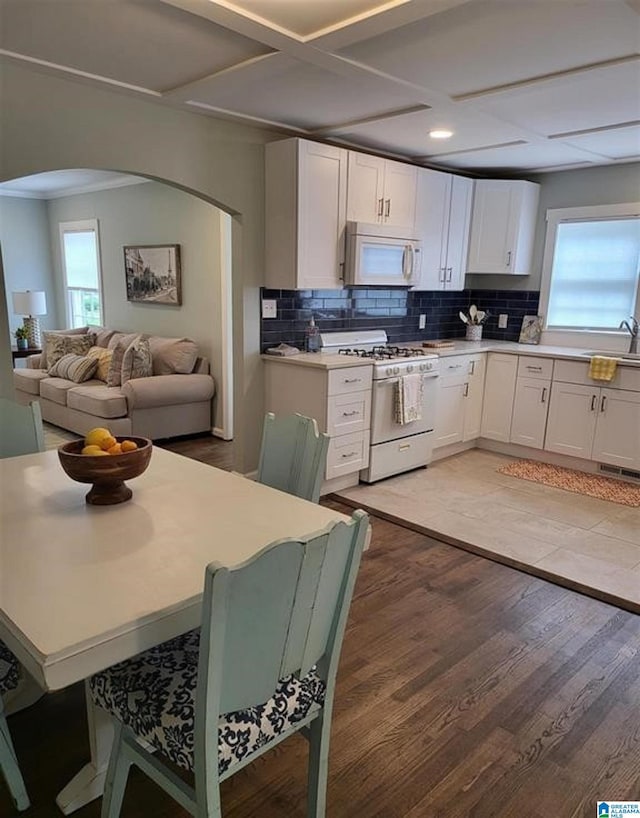 kitchen featuring backsplash, white cabinetry, white appliances, light wood-style floors, and arched walkways