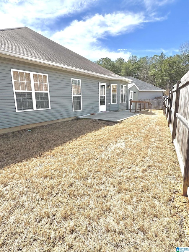 rear view of house with a shingled roof, a lawn, a fenced backyard, and a patio area