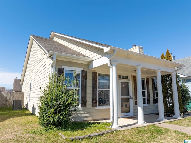 greek revival house with a shingled roof, a front lawn, fence, a porch, and a chimney