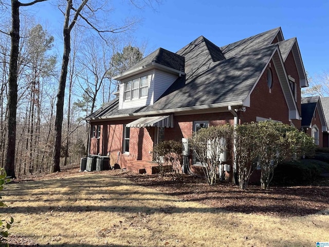 exterior space featuring brick siding, central AC, and roof with shingles