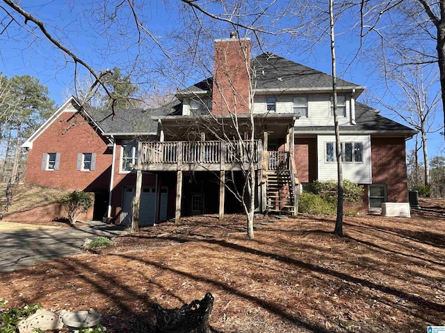 rear view of property featuring stairway, driveway, a chimney, a garage, and brick siding