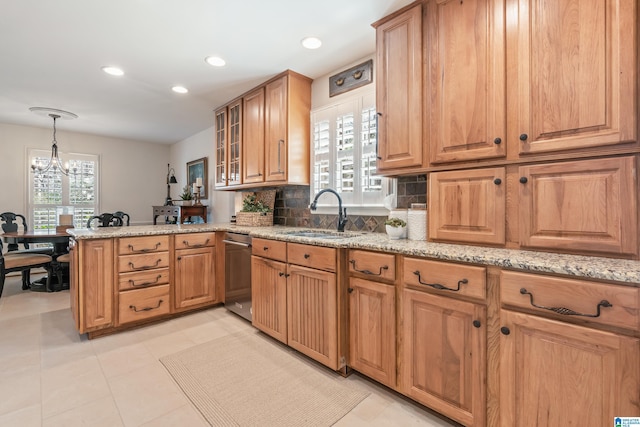 kitchen featuring light stone countertops, a peninsula, a sink, stainless steel dishwasher, and tasteful backsplash