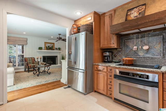 kitchen with a brick fireplace, decorative backsplash, stone counters, appliances with stainless steel finishes, and custom exhaust hood