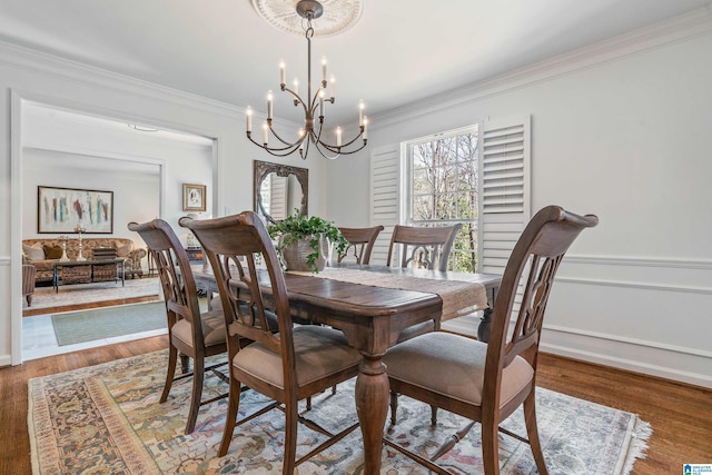 dining area featuring an inviting chandelier, wood finished floors, a wainscoted wall, and ornamental molding