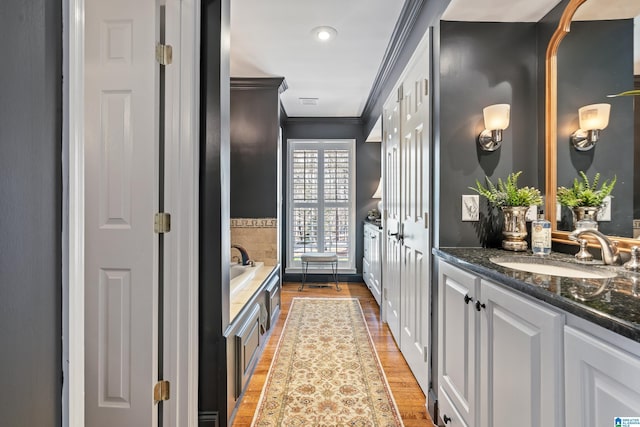 bathroom with ornamental molding, vanity, a garden tub, and wood finished floors