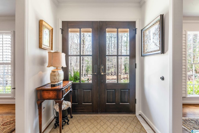 foyer featuring light wood finished floors, french doors, crown molding, and baseboards