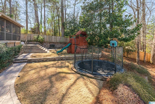 view of yard with a playground, a trampoline, a fenced backyard, and a sunroom