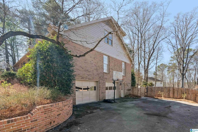 view of side of property with a garage, fence, brick siding, and driveway