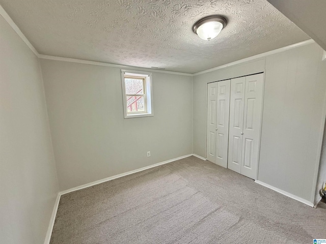 unfurnished bedroom featuring ornamental molding, a textured ceiling, a closet, carpet flooring, and baseboards