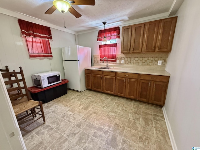 kitchen featuring tasteful backsplash, light countertops, brown cabinets, white appliances, and a sink