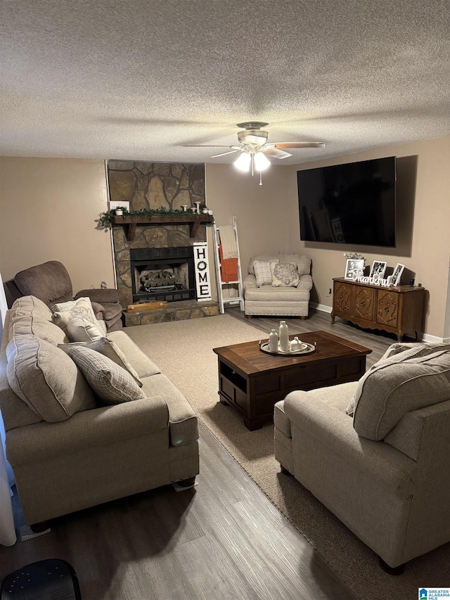 living area featuring baseboards, ceiling fan, a fireplace, wood finished floors, and a textured ceiling