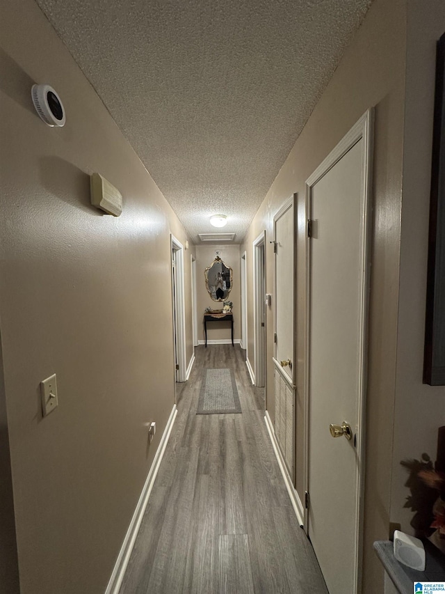 corridor featuring baseboards, dark wood-style flooring, and a textured ceiling