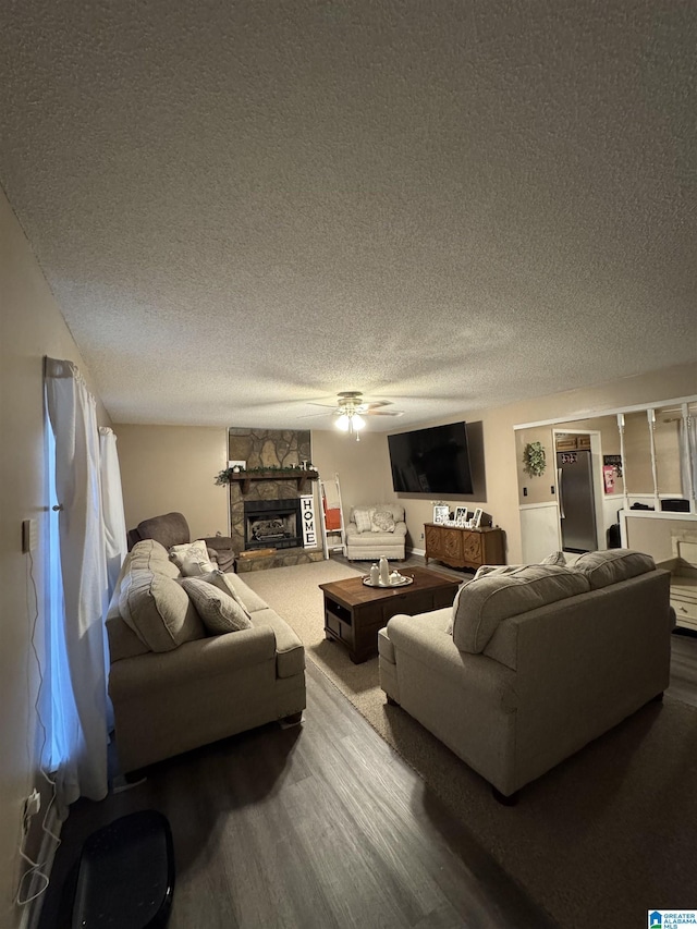 living area featuring a stone fireplace, a ceiling fan, wood finished floors, and a textured ceiling