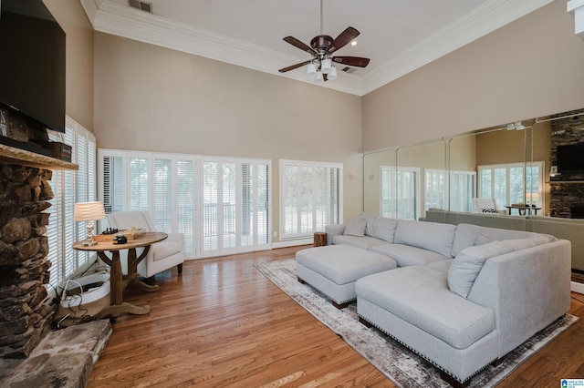 living room with wood finished floors, a high ceiling, a stone fireplace, crown molding, and ceiling fan