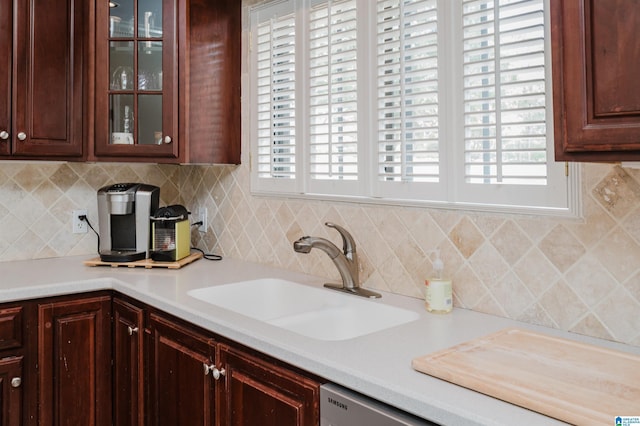 kitchen featuring glass insert cabinets, decorative backsplash, light countertops, and a sink