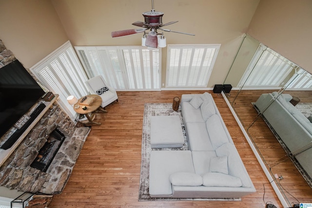 living room with a fireplace, a high ceiling, a ceiling fan, and wood finished floors