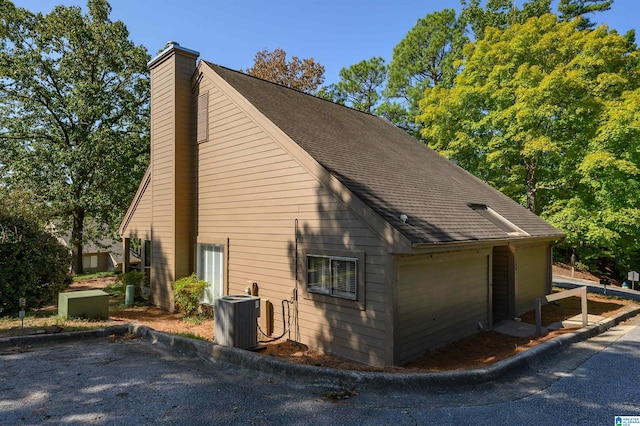 view of side of property with cooling unit, roof with shingles, and a chimney