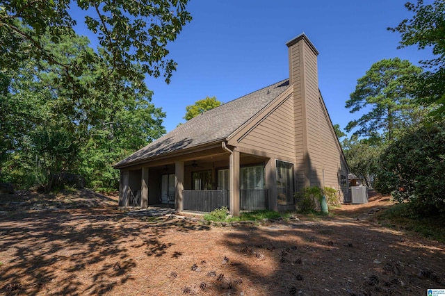 view of side of home featuring cooling unit, a chimney, and a shingled roof