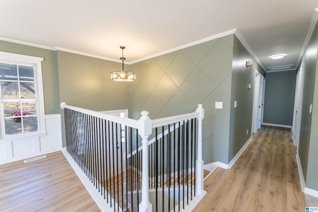 hallway featuring visible vents, light wood finished floors, baseboards, crown molding, and an upstairs landing