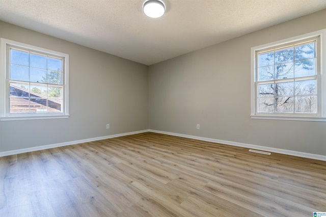 unfurnished room with visible vents, baseboards, light wood-style floors, and a textured ceiling