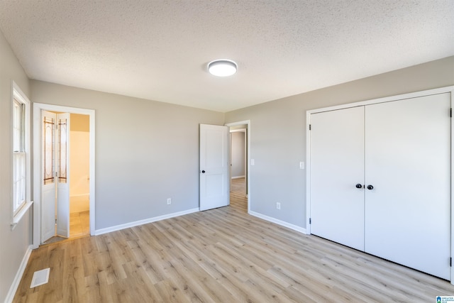 unfurnished bedroom featuring visible vents, a textured ceiling, a closet, light wood-style floors, and baseboards