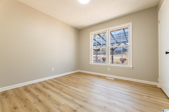 unfurnished room featuring a textured ceiling, visible vents, light wood-type flooring, and baseboards