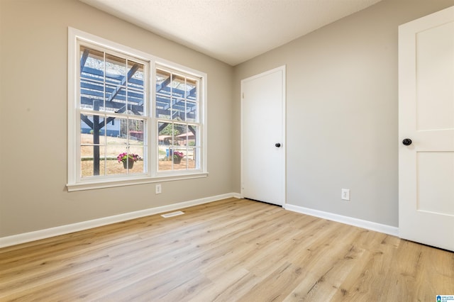 spare room featuring visible vents, baseboards, a textured ceiling, and light wood finished floors