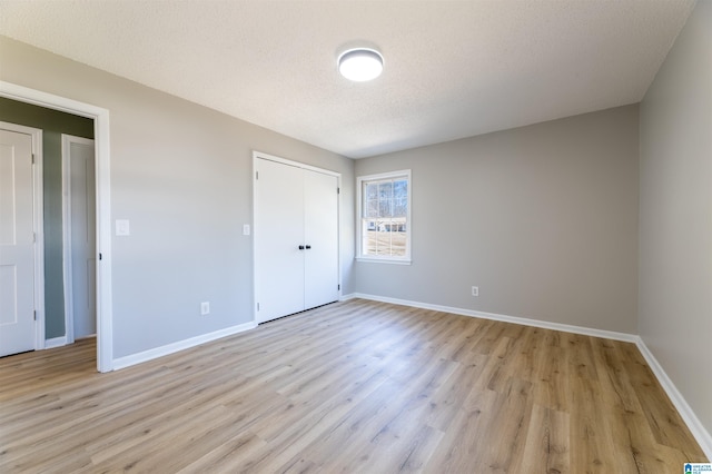 unfurnished bedroom featuring light wood-type flooring, baseboards, a textured ceiling, and a closet