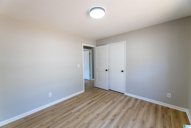 unfurnished bedroom featuring wood finished floors, baseboards, a closet, and a textured ceiling