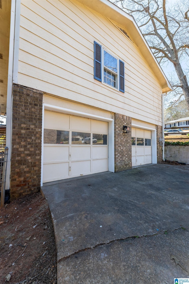 view of side of property featuring brick siding, an attached garage, and driveway